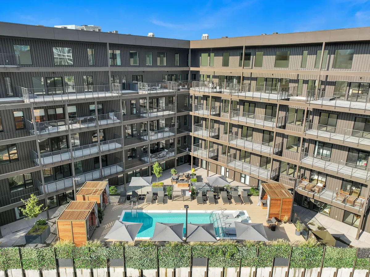 A vibrant exterior shot features a sparkling pool bordered by modern seating areas, lush landscaped greenery, and the backdrop of striking, contemporary architecture. The scene is lively yet serene, with ample space for community gatherings and sunset relaxation.