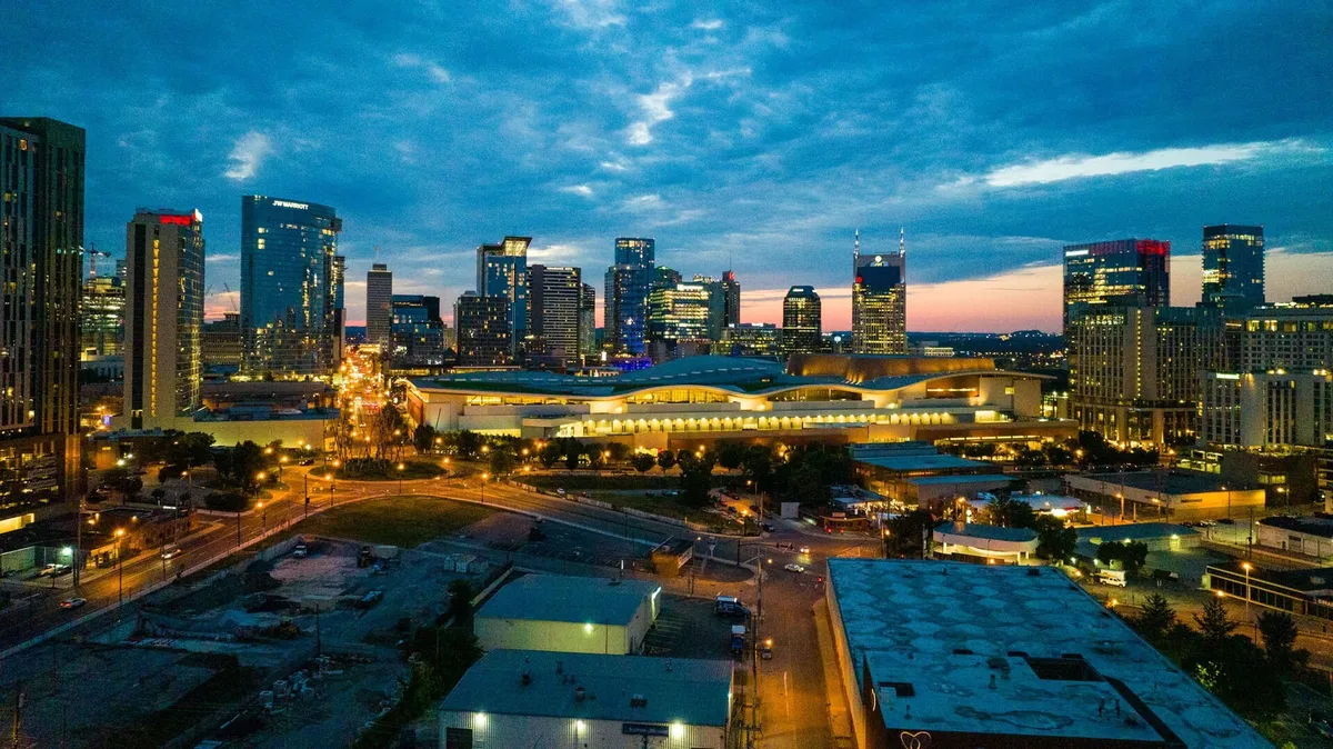 A sweeping city skyline at dusk with lights twinkling, entertainment venues visible, and the lively atmosphere of downtown. The streets are active, hinting at the nightlife and after-hours fun described in the section.