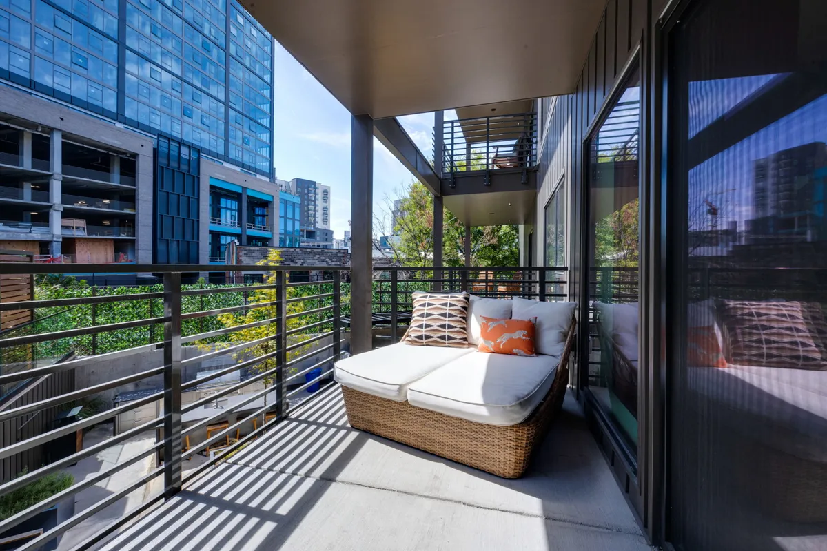 A stylish balcony setup with a modern lounge chair, railings, and a panoramic view of the city skyline. The seating area is designed for comfort, with plenty of natural light and an open-air feel that invites morning coffee or evening reflection.