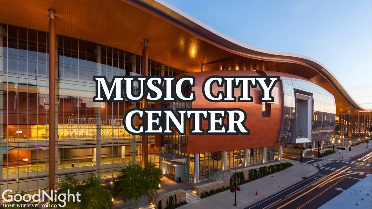 A modern event venue with striking glass windows and a curved roofline, the landscaped entrance is bustling with people attending a variety of events and conferences. The energetic atmosphere hints at its proximity to major city attractions and gathering spaces.