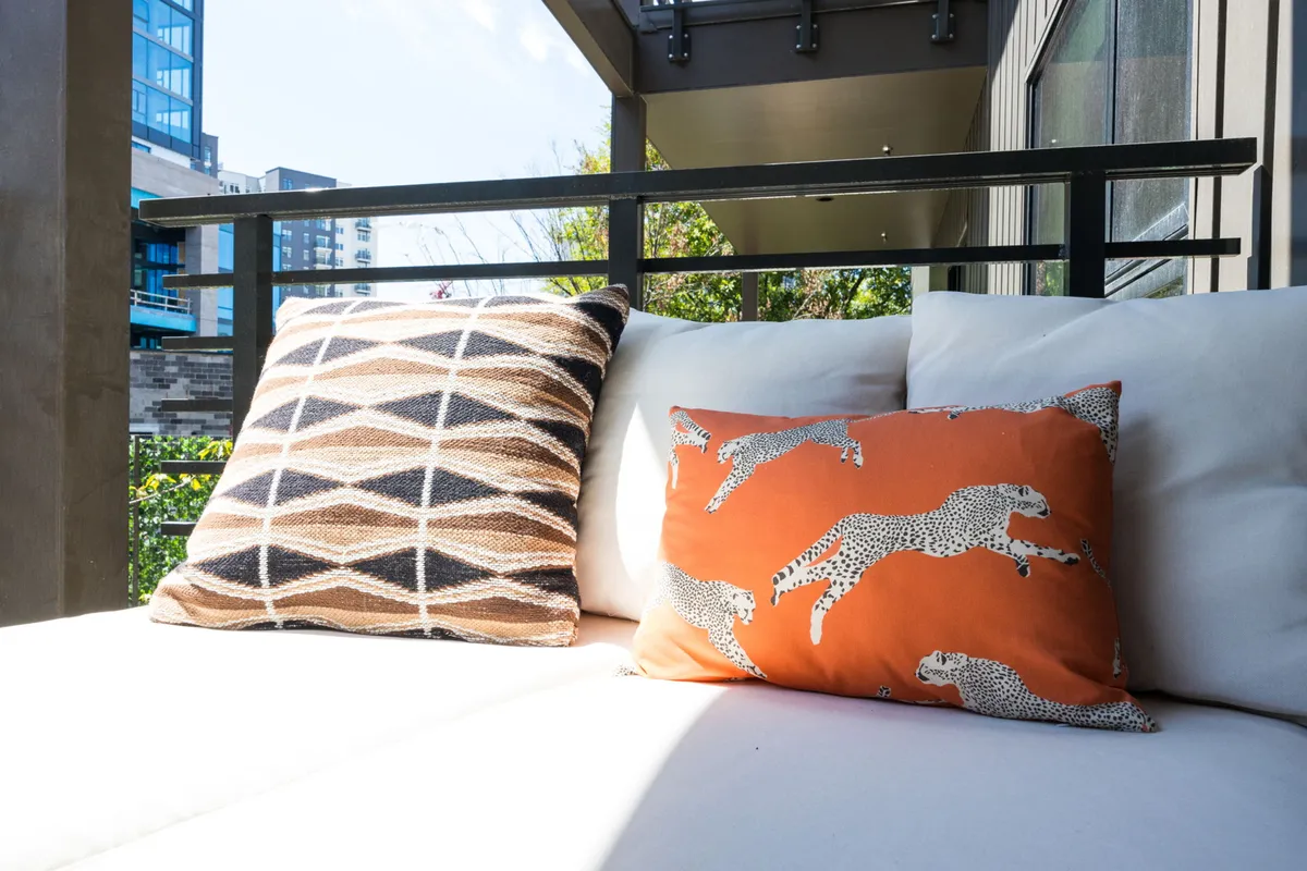 This image features a private balcony with comfortable outdoor seating and decorative pillows, offering a cozy space to relax. The balcony provides a clear view outward, suggesting both a vantage point over the city and a tranquil escape above the urban buzz.